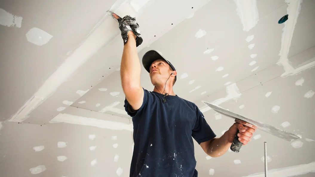 Drywall finisher smoothing joint compound on a ceiling overhead