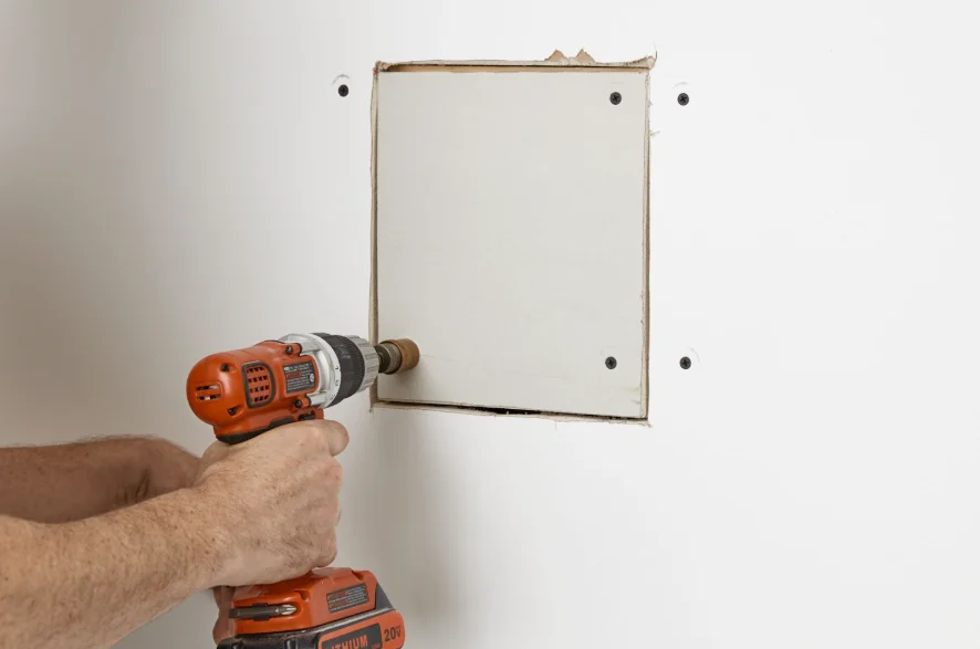 Cut-in drywall patch being screwed into place over a hole in a wall