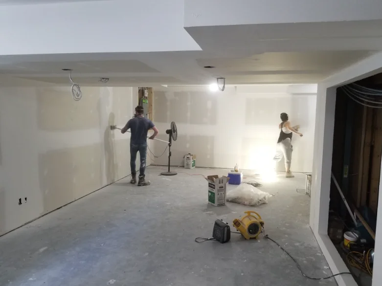 Two drywall finishers taping and mudding seams in a basement finish