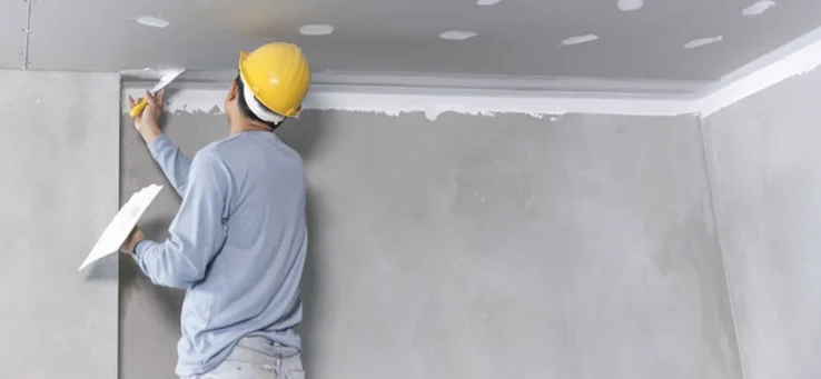 Drywall finisher applying compound along the joint where the wall meets the ceiling