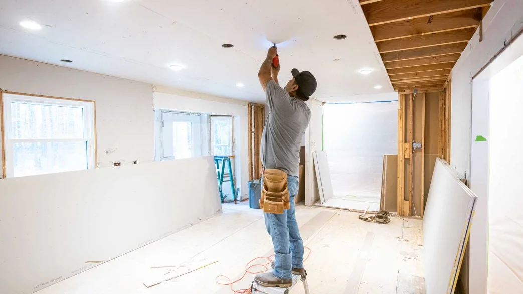 Installer on a step ladder fastening a new drywall panel to the ceiling