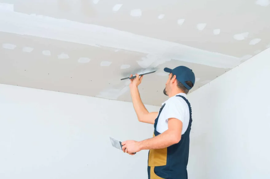 Drywall finisher applying joint compound over a taped ceiling seam